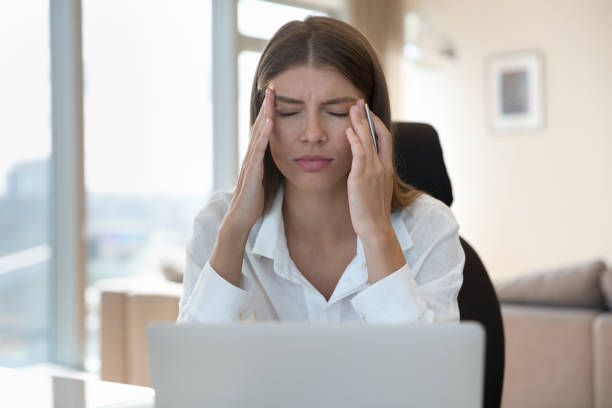 Woman work on laptop touching temples, suffers from headache stock photo