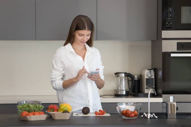 istock Woman standing in kitchen holds smartphone search recipe on internet 1756587953
