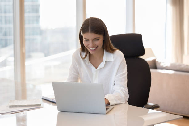 istock Woman using laptop seated at desk in modern skyscraper homeoffice 1756590179