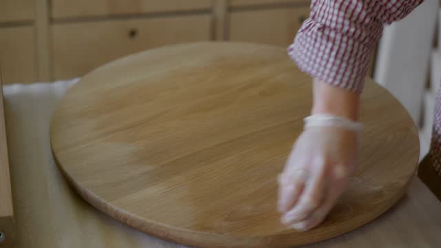 A close-up of a woodworker's hand processes the tabletop of a tea table with oil