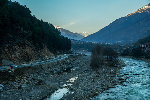 Highway next to Kulla Himachal Pradesh and Snowcapped Himalayas  mountainsin distance. Driving on the right hand side in India. Beas\n river valley and some villager upper Kullu town