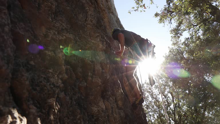 Athletic man climbs an overhanging rock with rope and carabiners, lead climbing.