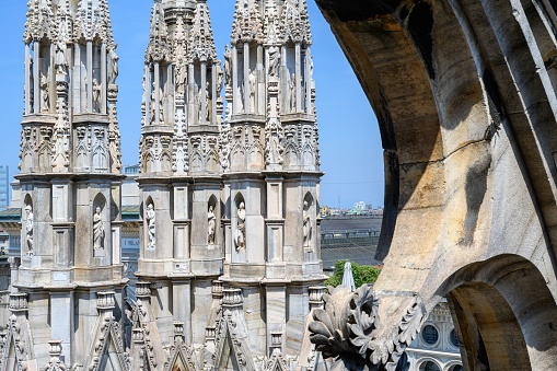 View of the various sculptures on the columns from the roof top of the Milan Cathedral with blue sky background and Milan city.