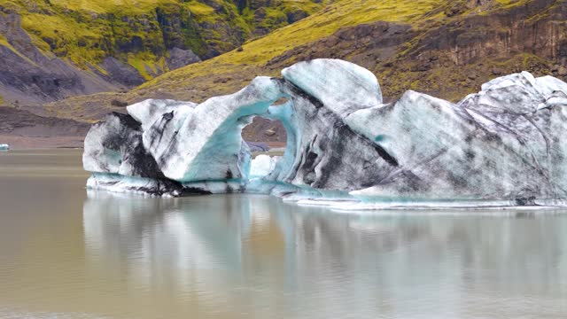 Rotation of a blue and black glacier in the water of a melting lake