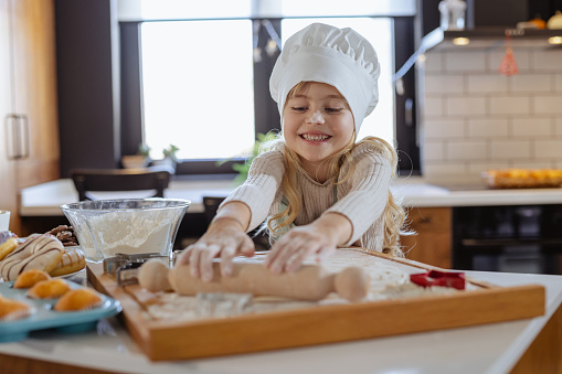 A cute girl with blond hair and chef's hat making cookie dough in the kitchen.