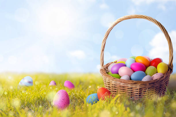 istock Wicker basket with painted Easter eggs in sunlit green grass, space for text 1756680785