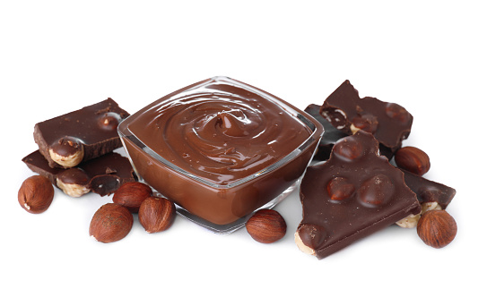 Chocolate pieces, bowl of sweet paste and hazelnuts on white background
