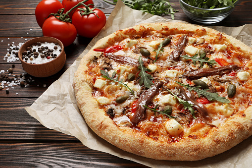 Tasty pizza with anchovies and ingredients on wooden table, closeup