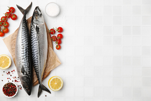 Raw mackerel, tomatoes and peppercorns on white tiled table, flat lay. Space for text