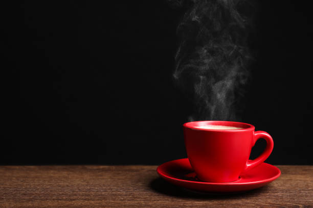 istock Red cup with hot steaming coffee on wooden table against black background, space for text 1756697123