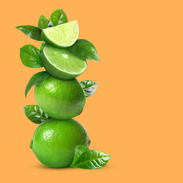 istock Stacked cut and whole limes with green leaves on orange background, space for text 1756699811