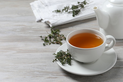 Aromatic herbal tea with thyme on white wooden table, space for text