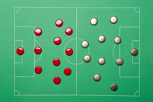 Football soccer game play tactic strategy scheme plan formation made of golden and red beer bottle caps on the bright solid fond plain green field background