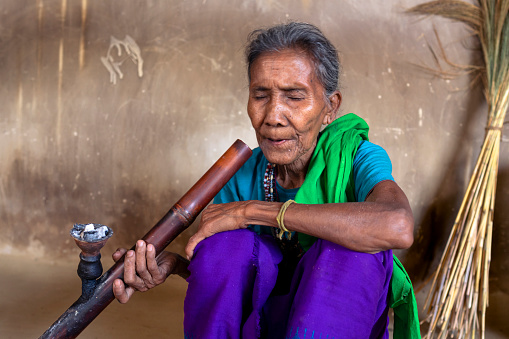 Portrait of an elderly Tripura woman in a small village in Bangladesh. She likes smoking in a traditional way.
