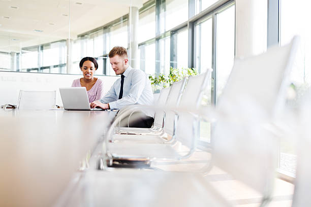 Two Young Business People in Modern Office Two young business people on a conference table with laptop discussing brightly lit stock pictures, royalty-free photos & images