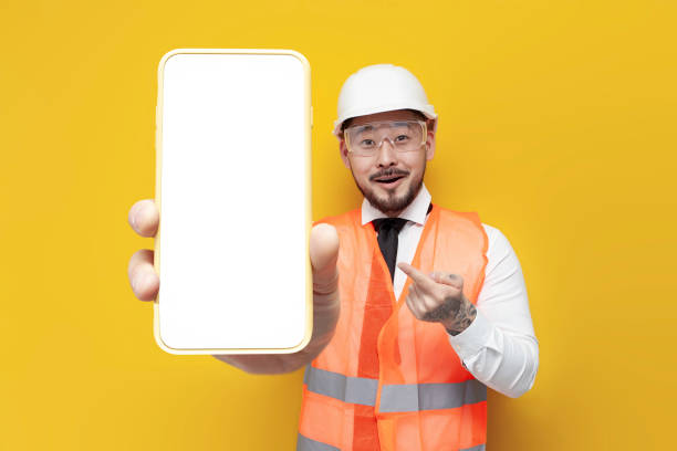 istock asian foreman in uniform showing blank smartphone screen on yellow isolated background, korean civil engineer 1756768610