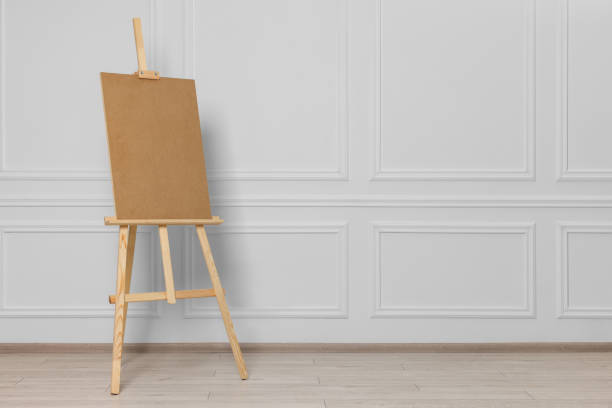 istock Wooden easel with blank board near white wall indoors. Space for text 1756770228