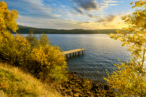 A colorful golden sunset above the mountains of North Idaho seen from a small lakeside lookout with a small wooden dock on the lake in Coeur d'Alene, Idaho USA.