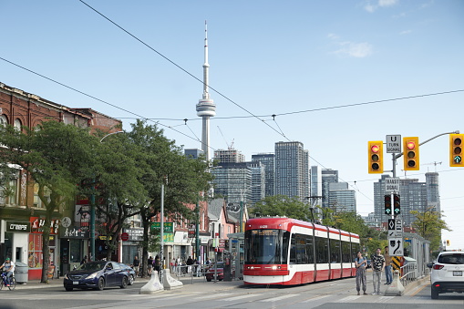 Toronto, Canada - August 27, 2023: A TTC 510 Spadina streetcar pulls up at the Spadina Avenue at Nassau Street stop in Chinatown. The CN Tower and upscale residential buildings of the Wellington Place neighbourhood stand in the background. Summer afternoon with clear skies.