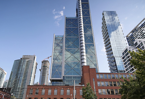 Toronto, Canada - August 27, 2023: Low angle view from the 400-block of Wellington Street West near Spadina Avenue. Upgraded historic buildings and modern towers line the Wellington Place district. Tower windows reflect clouds on a summer afternoon downtown.