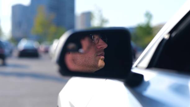 istock Happy young man sitting in the car while looking on the side view mirror, wearing glasses. Transport and lifestyle concept. Slow motion 1756811584