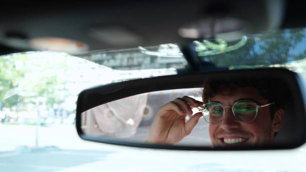 istock Male driver adjusting his glasses and looking in the rear view mirror while driving in a car in the city. Transport and lifestyle concept. Slow motion 1756811596