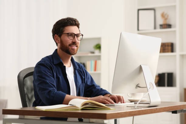 istock Home workplace. Happy man working with computer at wooden desk in room 1756816317