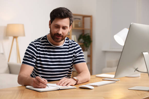 istock Home workplace. Man taking notes near computer at wooden desk in room 1756817375