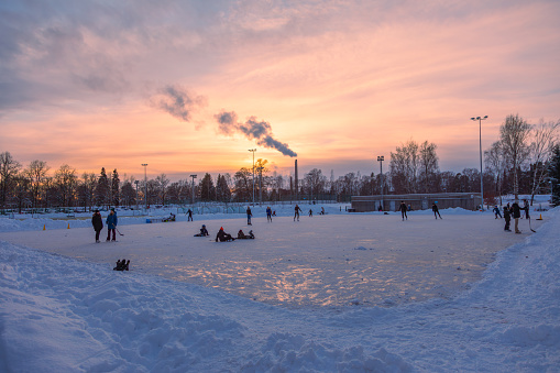 In the midst of a chilly Helsinki winter, people find joy in ice skating on a frozen soccer field as the sun sets. This heartwarming scene captures the essence of winter fun and community spirit.\nHelsinki, Cold Winter, Ice Skating, Frozen Soccer Field, People, Enjoyment, Community, Winter Fun, Cold Weather, Sunset.