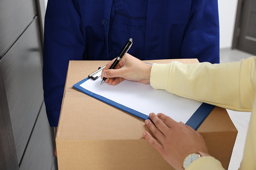 Woman signing for delivered parcel from courier indoors, closeup