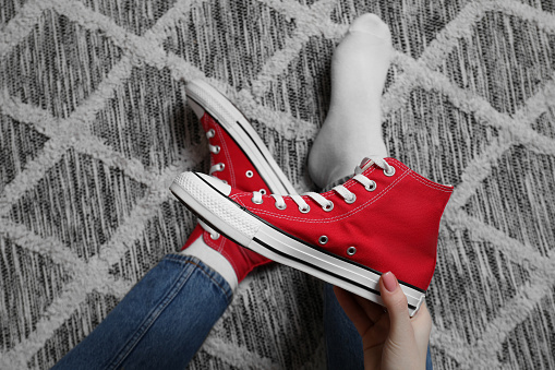 Woman with new stylish red sneakers sitting on carpet, top view