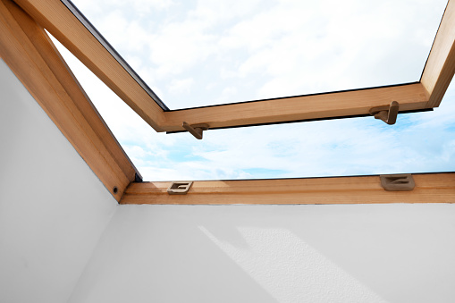 Beautiful view of cloudscape from open skylight roof window on slanted ceiling. Attic room