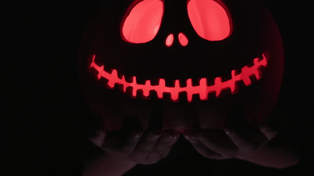 A young girl holds the Carved Jack O'Lantern in her hand, the Halloween pumpkin glowing in the dark.