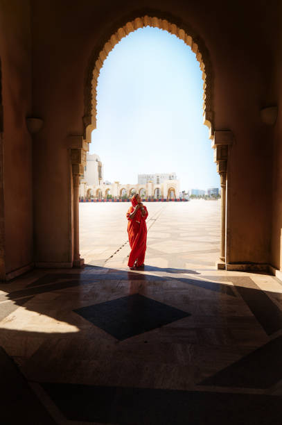 silueta de cuerpo entero de una mujer árabe musulmana con hiyab y ropa tradicional de pie bajo el arco de mármol de la mezquita - casablanca moroccan culture style islam fotografías e imágenes de stock