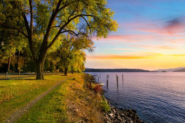 vista do pôr do sol do outono com cores de outono nas folhas ao longo do caminho arborizado da trilha do centenário enquanto faz o caminho ao longo do lago perto de silver beach em coeur d'alene, idaho eua. - dalene - fotografias e filmes do acervo