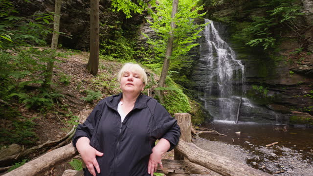 Mature woman relax on wooden trail near waterfall in Bushkill Falls, PA. Footage with push-panning camera motion