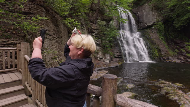 Tourist woman captures photos of forest and waterfall cascade in Bushkill Falls, PA. Rear view