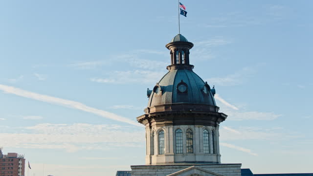 Condensation trail in blue sky above South Carolina State House dome in Columbia, SC. Close up. Aerial footage with descending-tilt up-forward camera motion