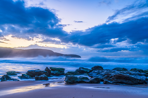 Moody sunrise at the seaside with clouds, rocks and waves at Killcare Beach on the Central Coast, NSW, Australia.
