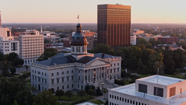 South Carolina State House stand amidst Business District of Columbia, SC at sunrise. Aerial footage with backwards-panning camera motion