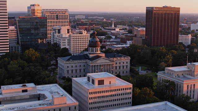 State Capitol Building hiding in Business District of Columbia in South Carolina in the morning. First Presbyterian Church towers over Downtown cityscape. Aerial footage with wide-panning-backwards camera motion