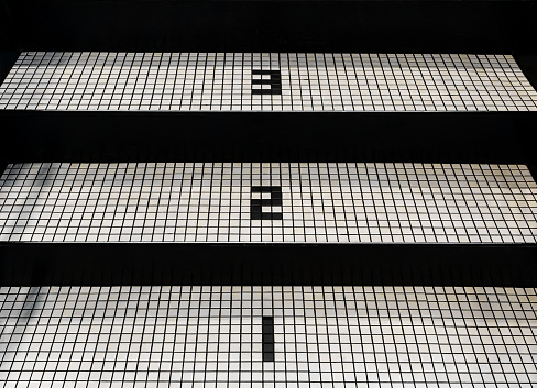 Old, worn black staircase with tiled, ascending steps numbered 1, 2, and 3. Small rectangular  discolored tiles.