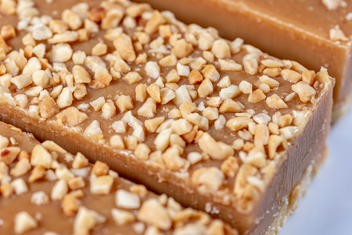 A piece of caramel slice covered with nuts on a white plate