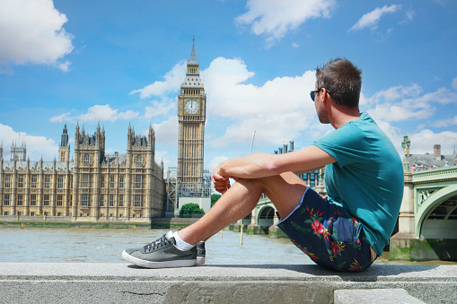 a young men tourist on a city trip in London looking at Big Ben at Westminster Bridge, a young man by the river Thames at the famous places in London, Big Ben and Westminster Bridge in London UK