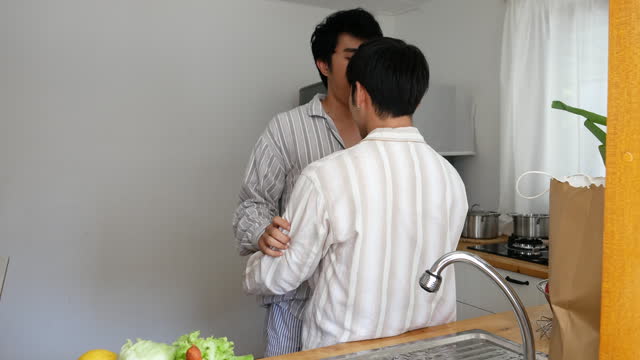Asian people happy time smile, laugh in kitchen. Asian gay couple homosexual cooking together in kitchen prepare fresh vegetable make organic salad healthy food. Best friend LGBTQ lifestyle concept