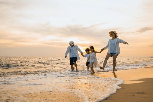 Happy family having fun running on a sandy beach at sunset time, Active parents and people father, mother, children son and daughter holding hands together walking on beach, tropical summer vacations