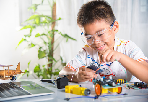 Asian kid boy plugging energy and signal cable to sensor chip with A.I. robot car, Little child remotely learn online with car toy, STEAM education AI technology course school learning lesson