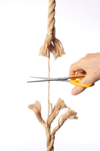 Close-up shot of cutting a brown rope with a scissors, isolated on white background.