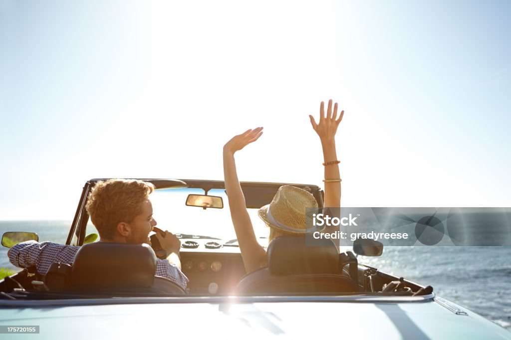 The perfect start to a holiday! A happy young couple parked by the ocean in a convertible on a sunny day Car Stock Photo