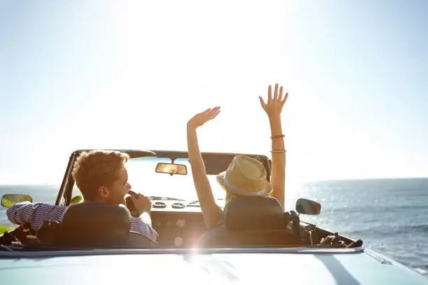 A happy young couple parked by the ocean in a convertible on a sunny day